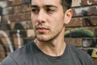 Homme avec un piercing au labret décalé en titane, look urbain devant un mur en briques